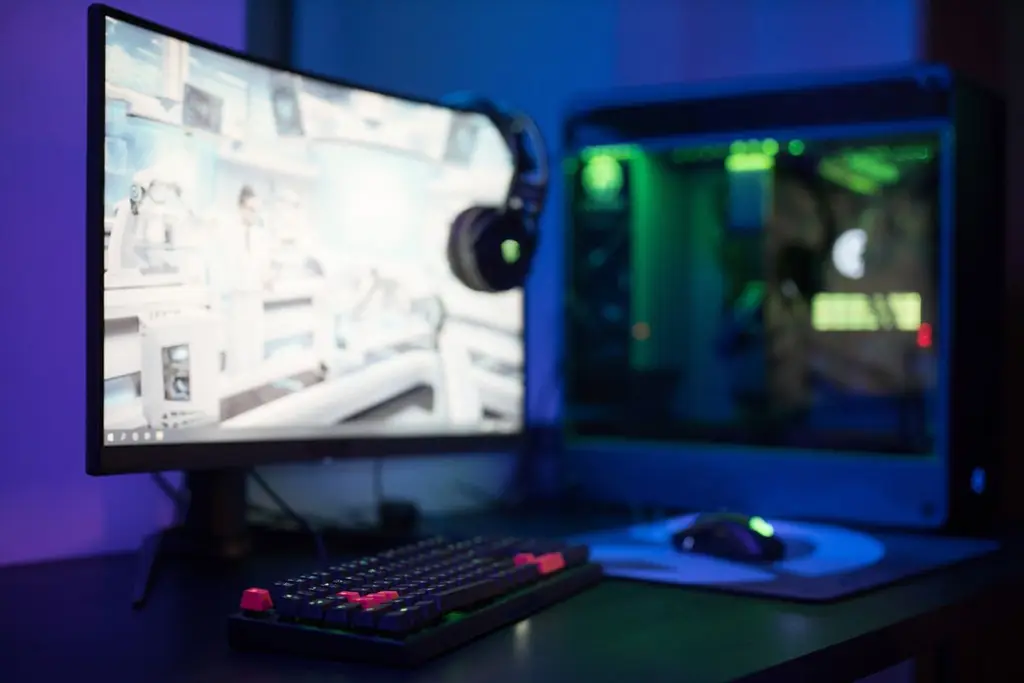 A curved gaming monitor on a desk with a keyboard and mouse in blue light