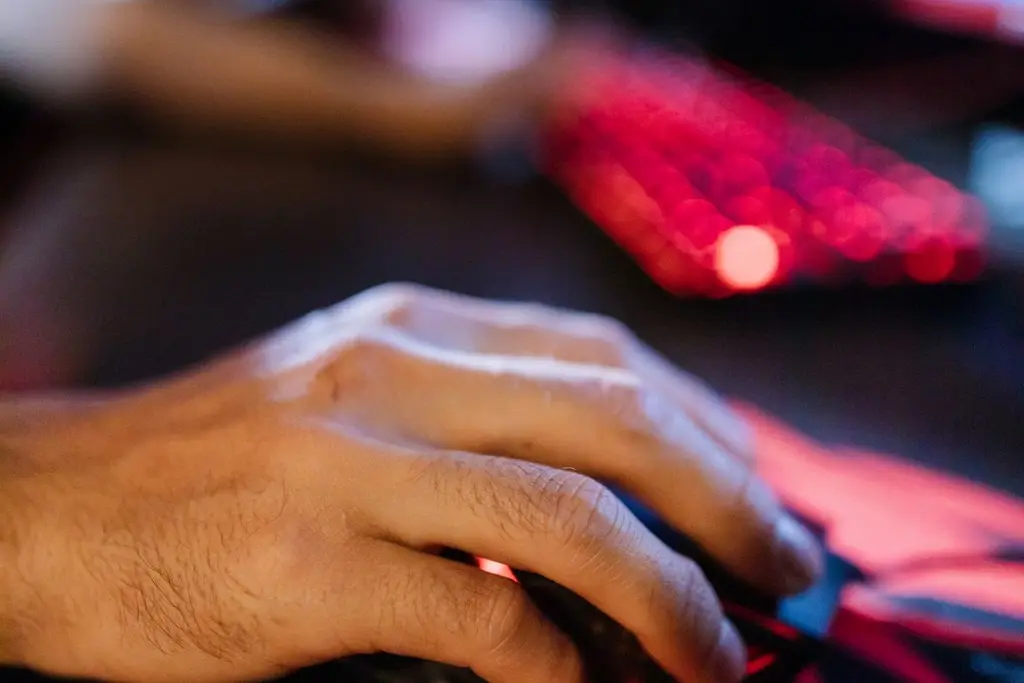 A hand on a gaming mouse in red keyboard light