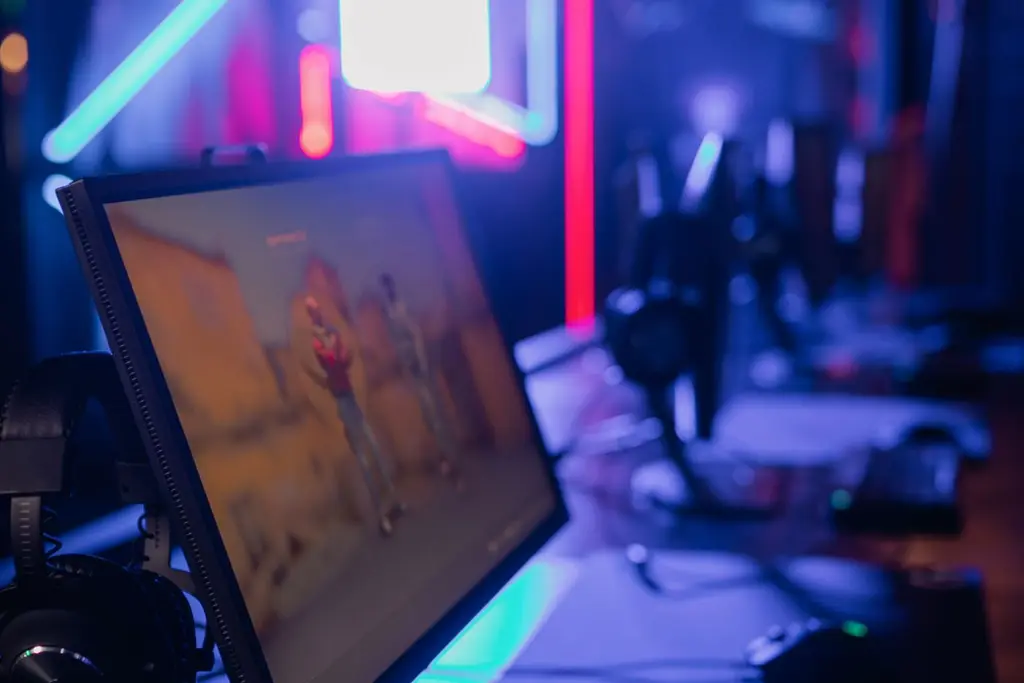 A gaming desk with a monitor and keyboard in neon light