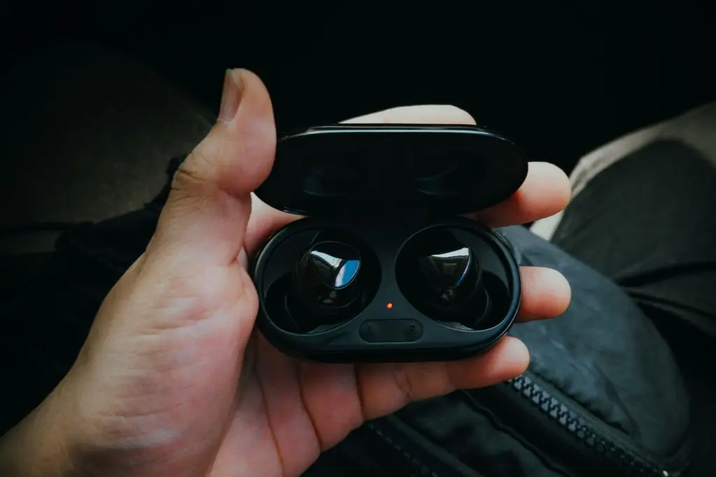 A hand holding a pair of wireless earbuds in an open charging case
