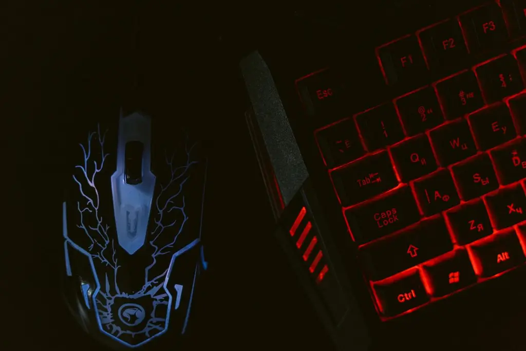 A glowing gaming mouse next to a red backlit keyboard