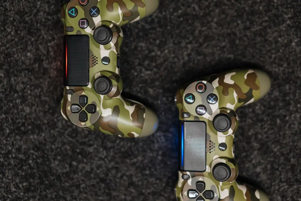 Two camouflage game controllers on a dark carpet