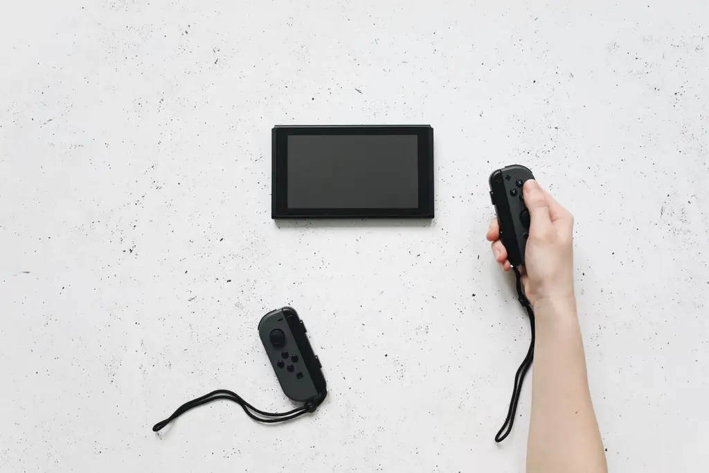 A hand holding a Joy-Con controller above a Nintendo Switch on a white surface