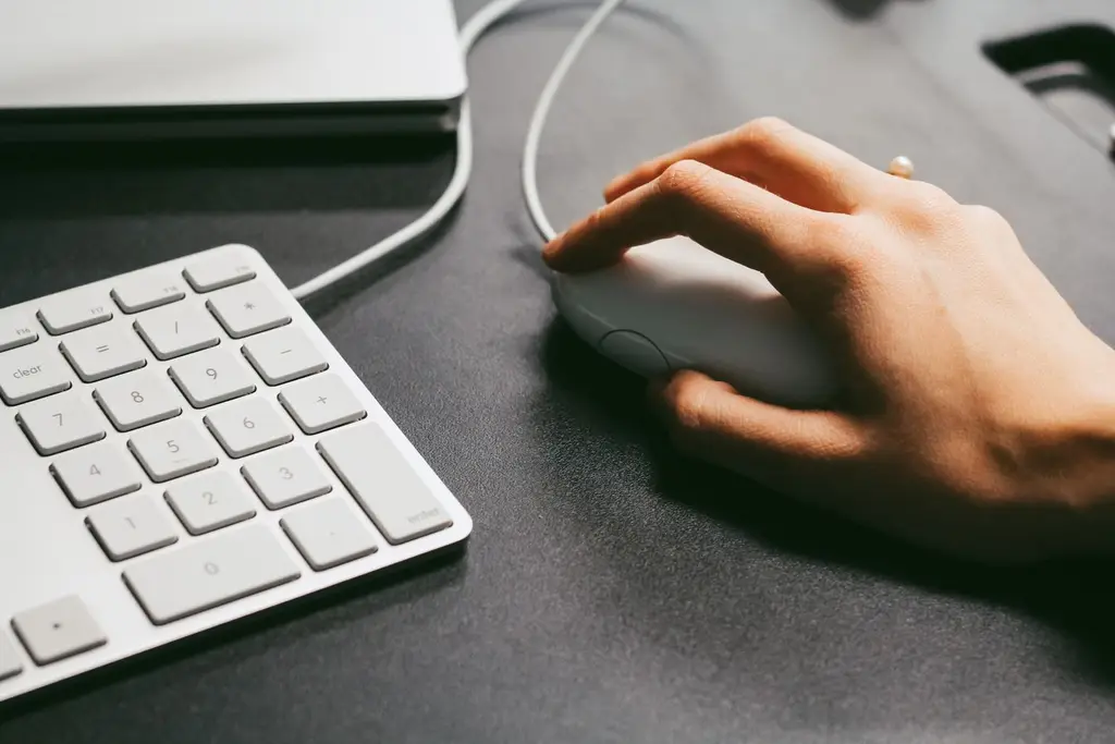 A hand resting on a computer mouse beside a keyboard